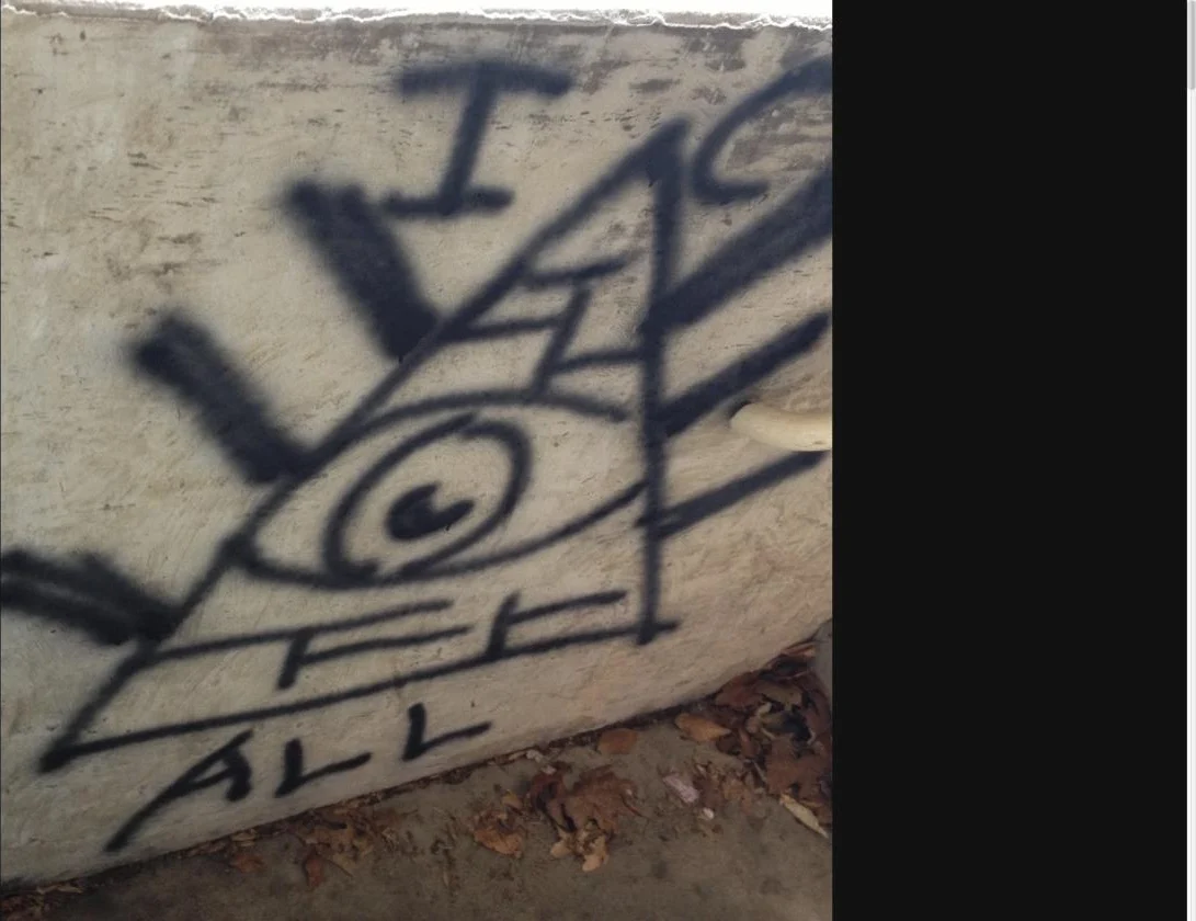 Street photography by Winston E. W. Cash: a hand-drawn eye inside a pyramid on a weathered concrete wall with the words I See All