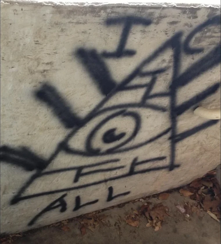 Street photography by Winston E. W. Cash: a hand-drawn eye inside a pyramid on a weathered concrete wall with the words I See All